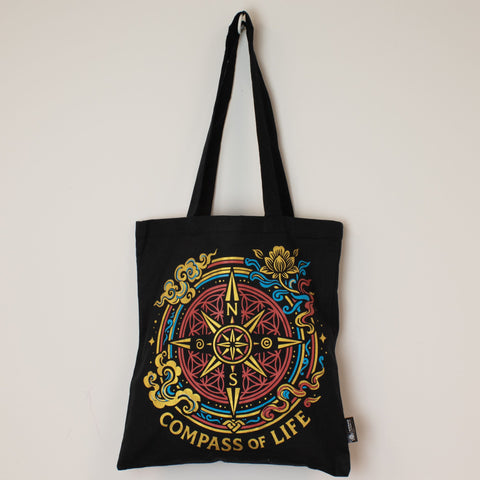 Front view of the black Compass of Life tote bag hanging against a plain light wall