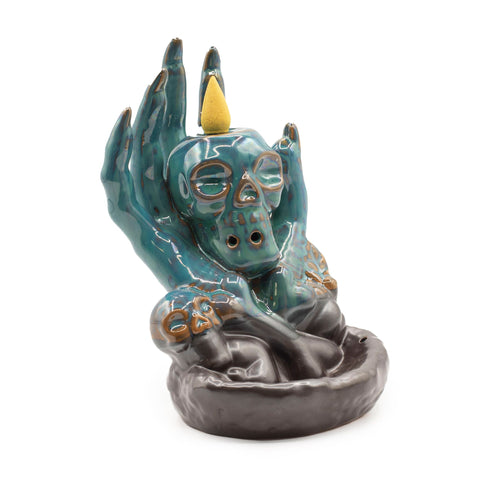 Backflow Incense Burner, Skull in Hand, glossy teal skull held by a raised hand above a grey dish