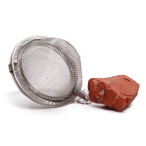 Close-up of the silver mesh tea strainer beside its rough red jasper stone on a white background