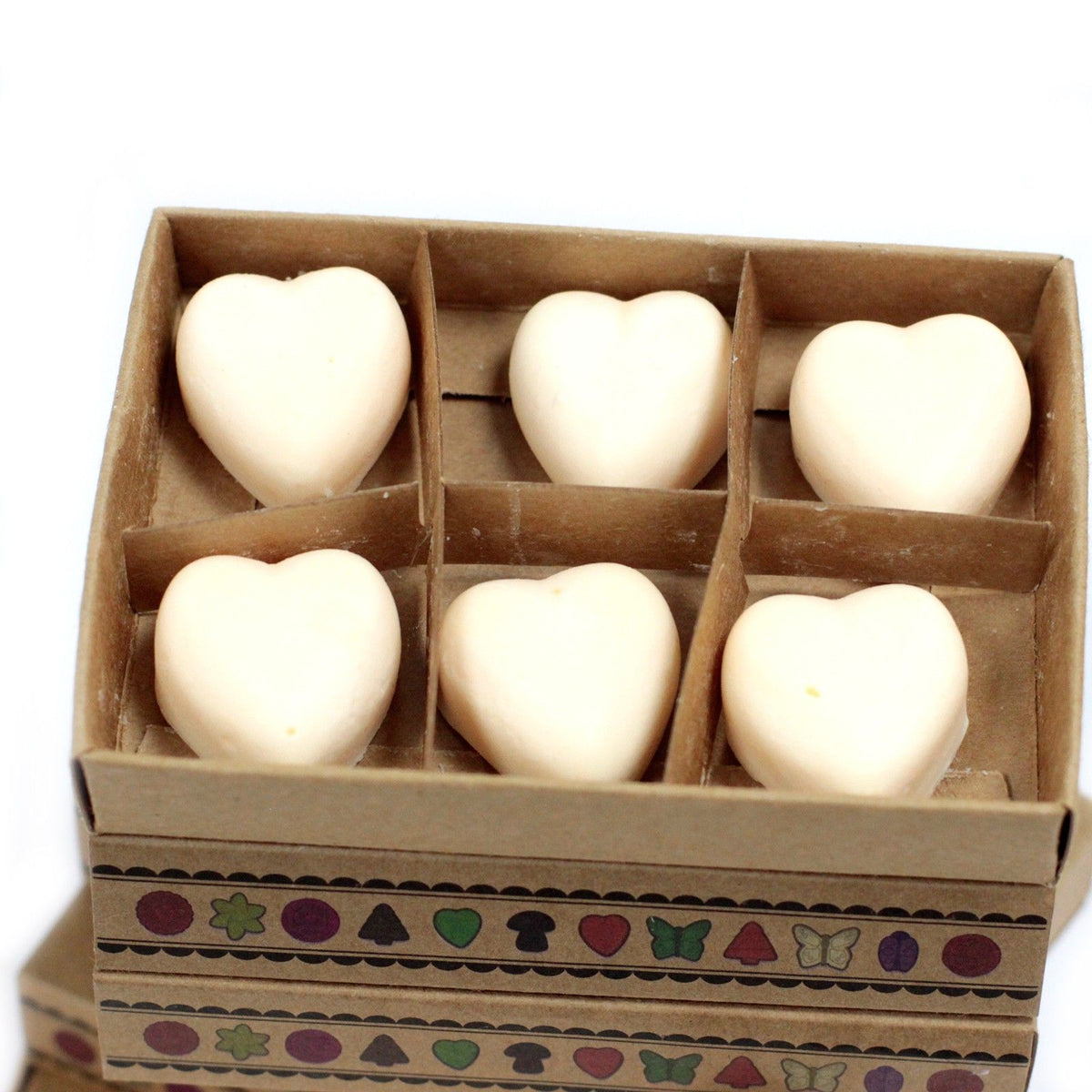 Heart-shaped wax melts in six compartments of an open cardboard box, viewed close up from the front