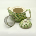 Green daisy teapot shown open with lid and metal strainer beside it