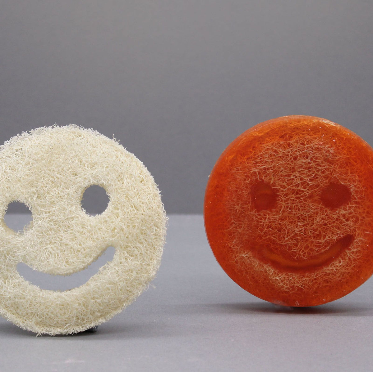 Happy Scrub Soap, Grapefruit, orange smiling round soap beside a pale cream smiling scrubber