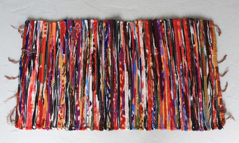 Multicoloured striped rug laid flat on a pale floor, shown from above with loose fringe at the edges
