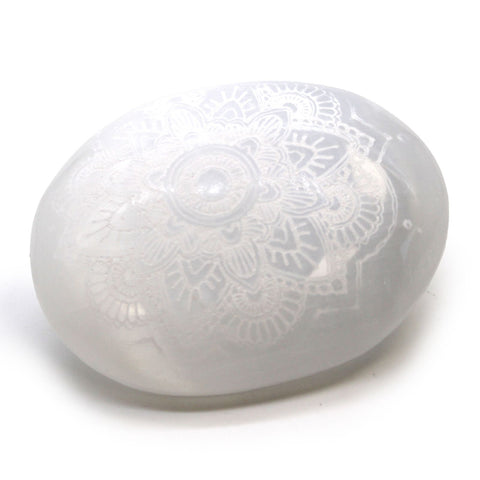 Mandala engraved selenite palm stone shown at an angle on a white background, with light across its surface