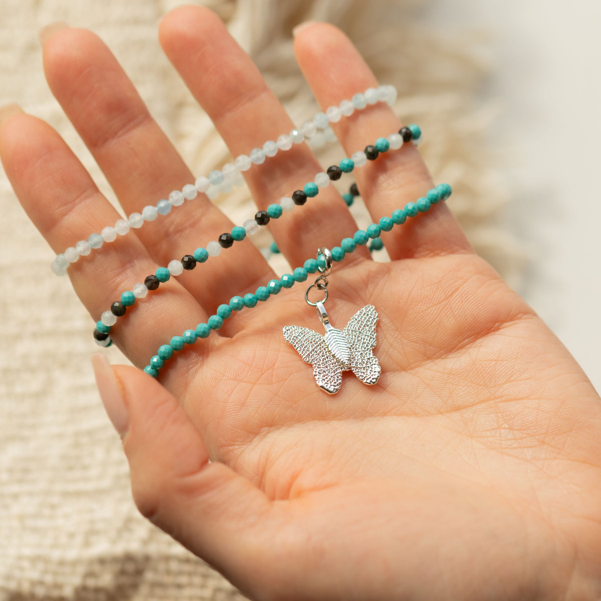 Three bracelets and butterfly charm displayed in a hand