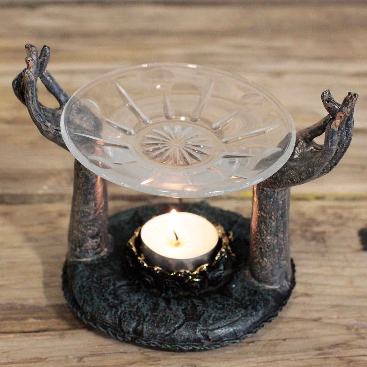 Om Hands Oil Burner: two open bronze-finish hands holding a glass dish, on a dark green base
