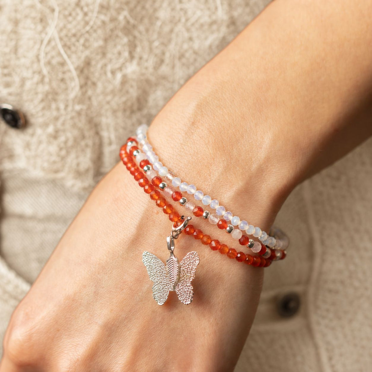 Close view of the layered bracelets and butterfly charm on a wrist
