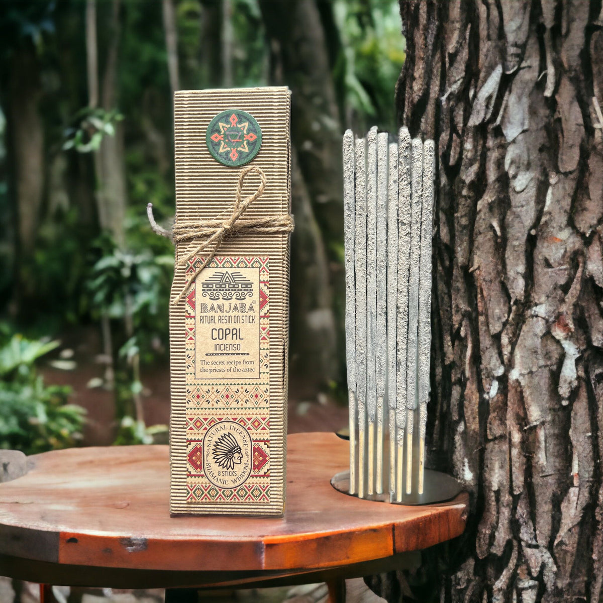 Ritual Resin on Stick, Copal, a patterned box and upright grey sticks on a wooden table beside a tree