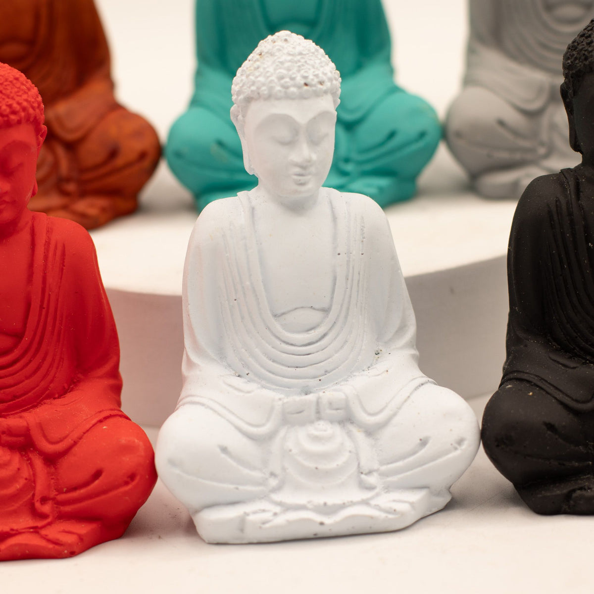 Matt Mini Buddha, white seated figure shown close up among red, teal, grey and black figures