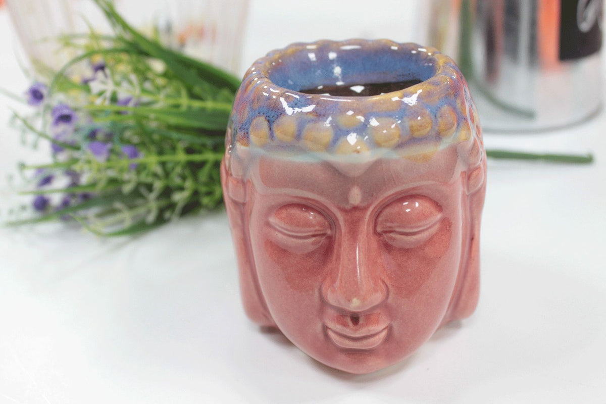 Buddha Oil Burner, Rose & Teal, shown from the front on a white surface beside flowers