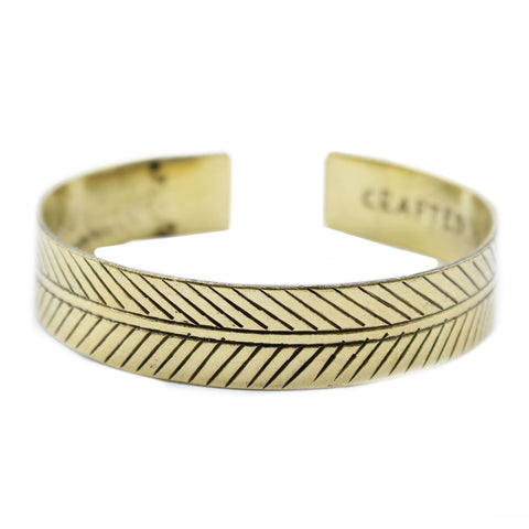 Close-up of the open brass cuff against a white background, with diagonal leaf engraving