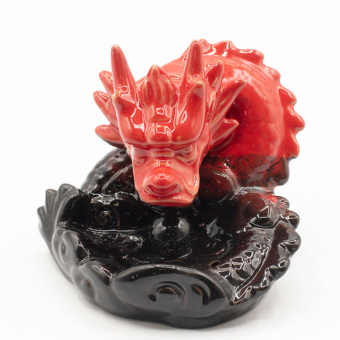 Small red dragon incense burner shown head-on, with its black patterned base against white