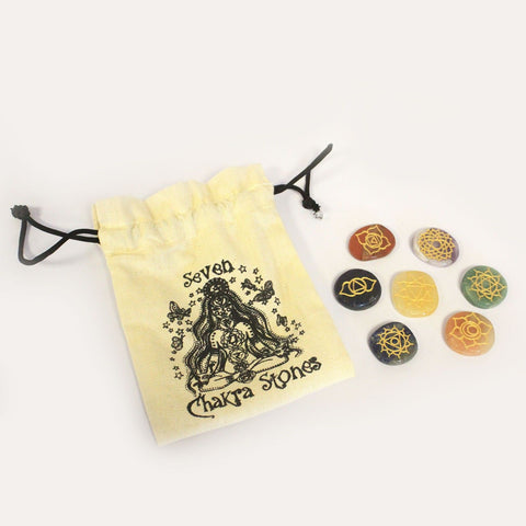 Seven engraved chakra stones next to their printed cotton pouch