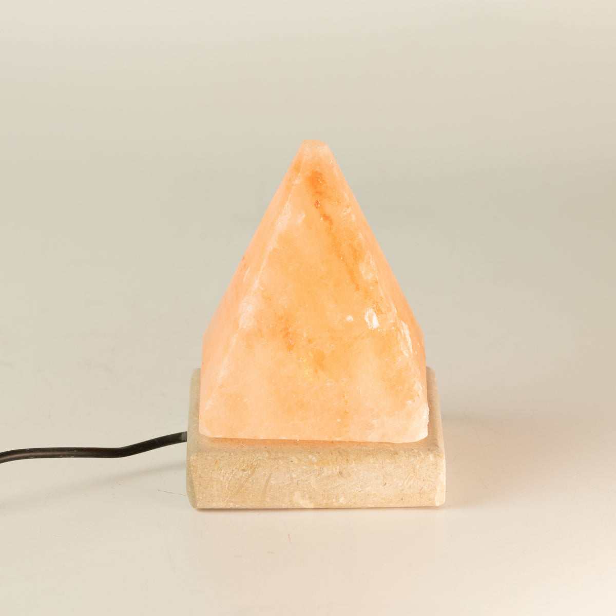 Front view of the pyramid salt lamp on its pale square base, cable visible against a plain background