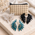 Pearl, jet black and teal glass angel wing earrings with a woven fabric zip pouch on a stone slab