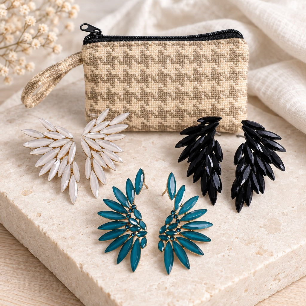 Pearl, jet black and teal glass angel wing earrings with a woven fabric zip pouch on a stone slab